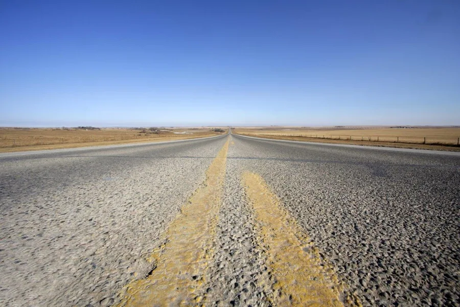 Long straight highway with yellow center line disappearing into desert horizon under clear blue sky