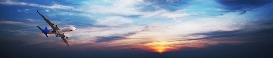 Commercial aircraft flying through dramatic sunset sky with golden and blue clouds at dusk.