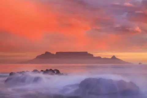 Dramatic sunset over Table Mountain with waves and mist at golden hour