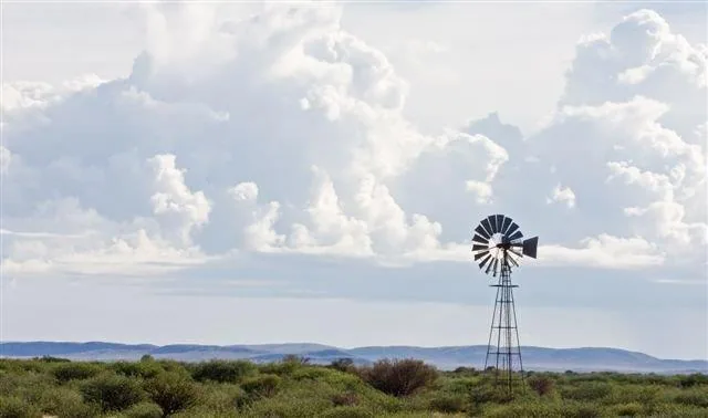 Windmill standing in arid bushland with puffy white clouds and mountains on horizon