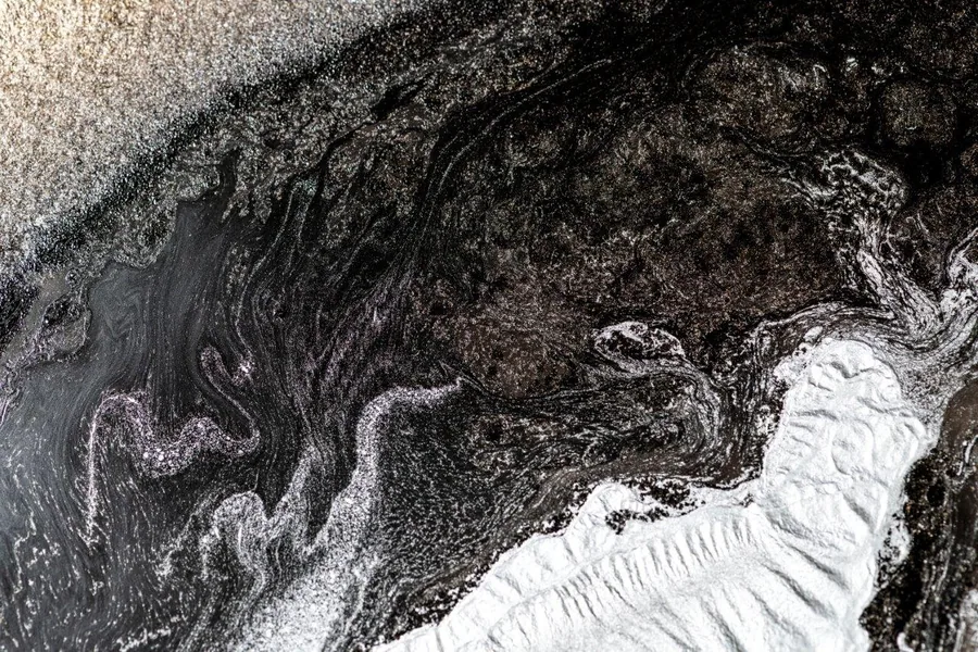 Abstract swirling pattern in black, white, and grey resembling flowing molten metal or liquid marble texture.