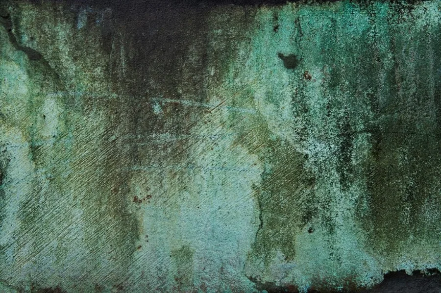 Weathered metal surface with green patina, rust stains, and textured oxidation marks.