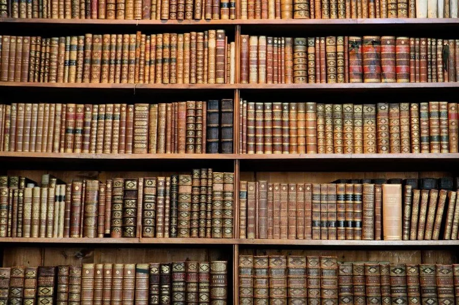 Rows of antique leather-bound books with decorative spines arranged on wooden shelves.