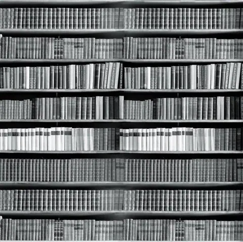 Black and white repeating pattern of book spines on shelves creating a library wall texture.